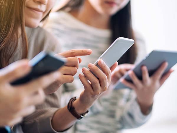 Zwei junge Frauen nutzen Smartphone bzw. ein Tablet. Man kann ihre Gesichter nicht erkennen