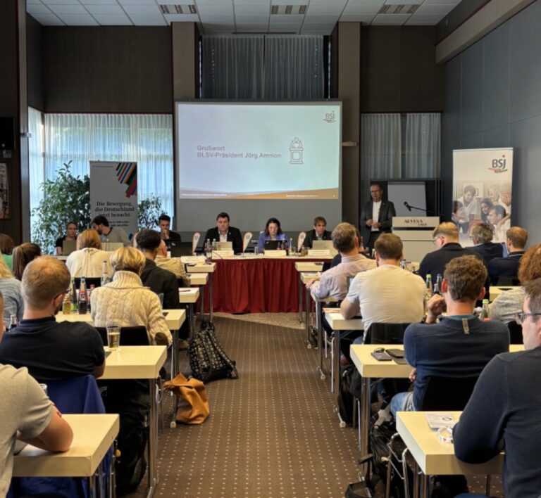 Personen sitzen in einem Saal und hören bei einer Präsentation zu