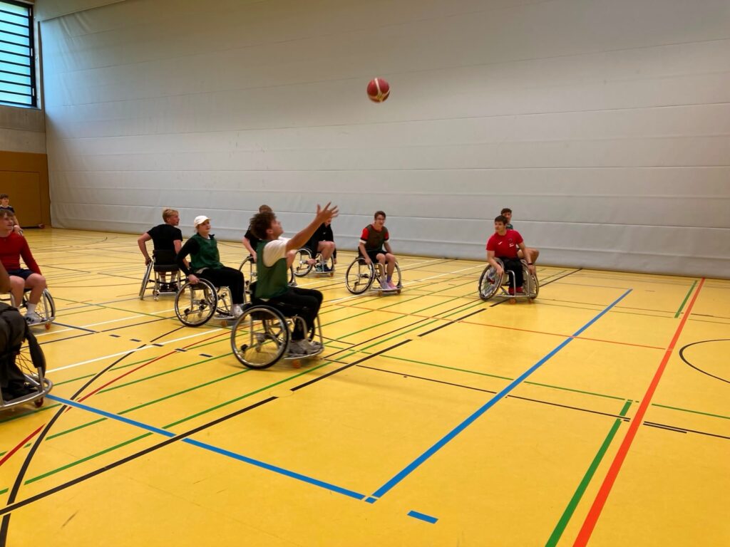 Eine Gruppe Freiwilligendienstleistender spielt in einer Turnhalle Rollstuhlbasketball.